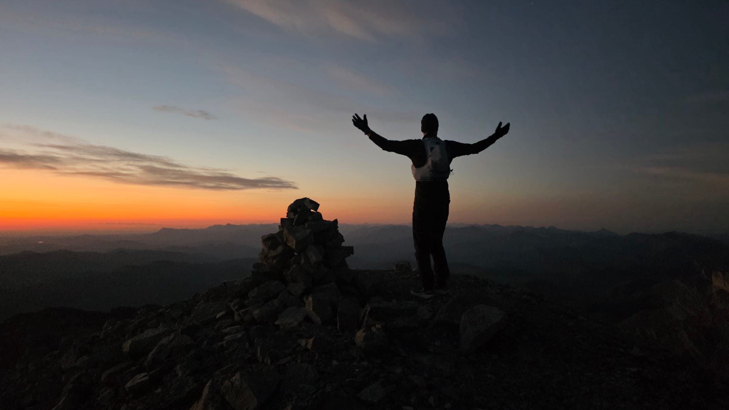 Shep with arms raised on a mountaintop at sunrise in the Canadian Rockies